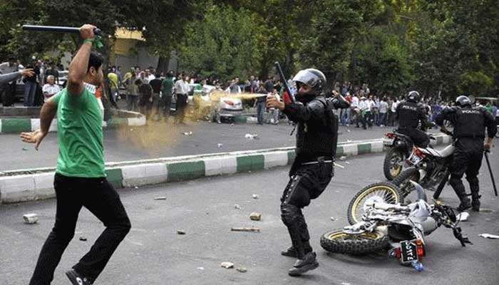 ایران میں مظاہرے کے دوران پولیس اہلکار اور نوجوان نے ایک دوسرے پر لاٹھیاں تان رکھی ہیں۔