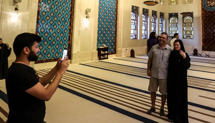 کینیڈین جوڑا ڈورینیل اور کلارا پوپا، دوحہ کے کٹارا ثقافتی ضلع میں عثمانی طرز کی نیلی مسجد کا دورہ کرتے ہوئے تصویر بنوا رہے ہیں۔ تصویر بشکریہ:اے ایف پی