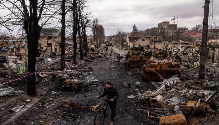 جنگ سے تباہ حال ایک یوکرینی سڑک، شہری سائیکل پر گزر رہا ہے۔