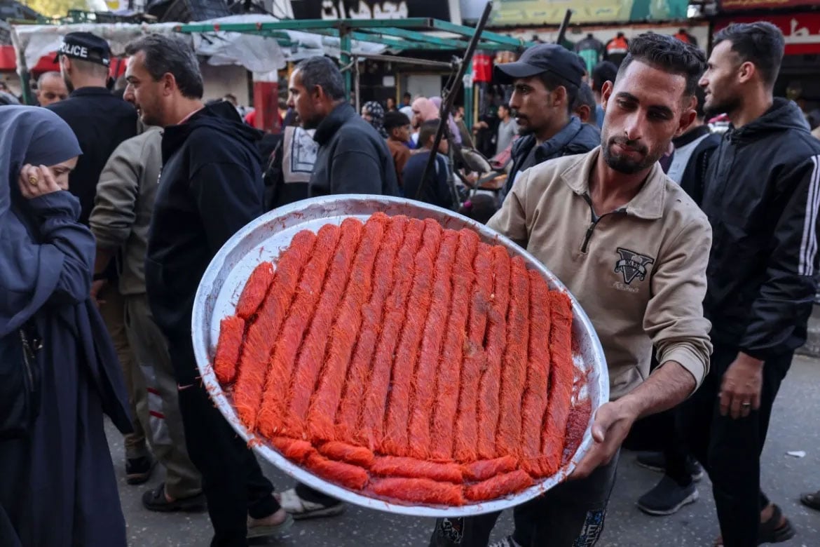 رفح کے ایک بازار میں ایک فلسطینی شخص مٹھائی کی ٹرے دکھا رہا ہے۔ [محمد عابد/اے ایف پی]