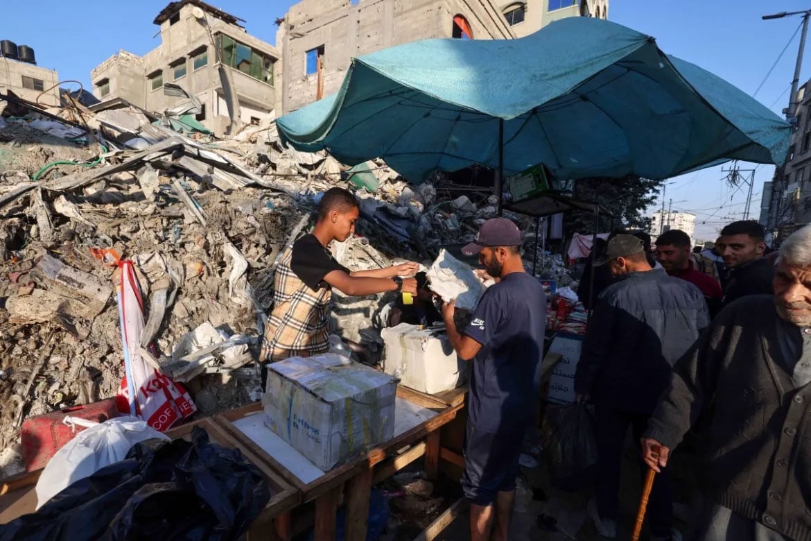 فلسطینی عید الفطر کے موقع پر جنوبی غزہ کی پٹی کے رفح میں اسرائیلی حملے میں تباہ کی گئی عمارت کے سامنے سامان فروخت کر رہے ہیں۔ [محمد عابد/اے ایف پی]
