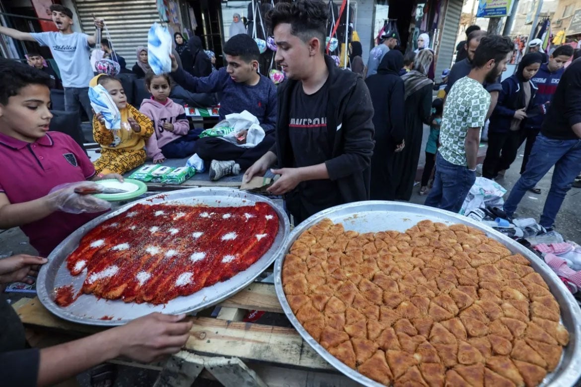 نوجوان فلسطینی دکاندار کھلے بازار میں مٹھائیاں فروخت کر رہے ہیں، یہاں لاکھوں بے گھر فلسطینی خیموں کے کیمپوں میں رہتے ہیں۔