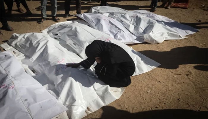 ایک فلسطینی خاتون شہداء کی لاشوں کے قریب بیٹھی نوحہ کناں ہیں—تصویر بشکریہ سوشل میڈیا
